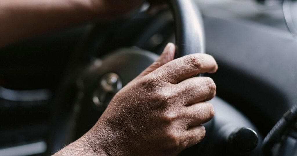 Mão de um motorista apoiada com calma no volante, interior de carro, tema pontos na CNH