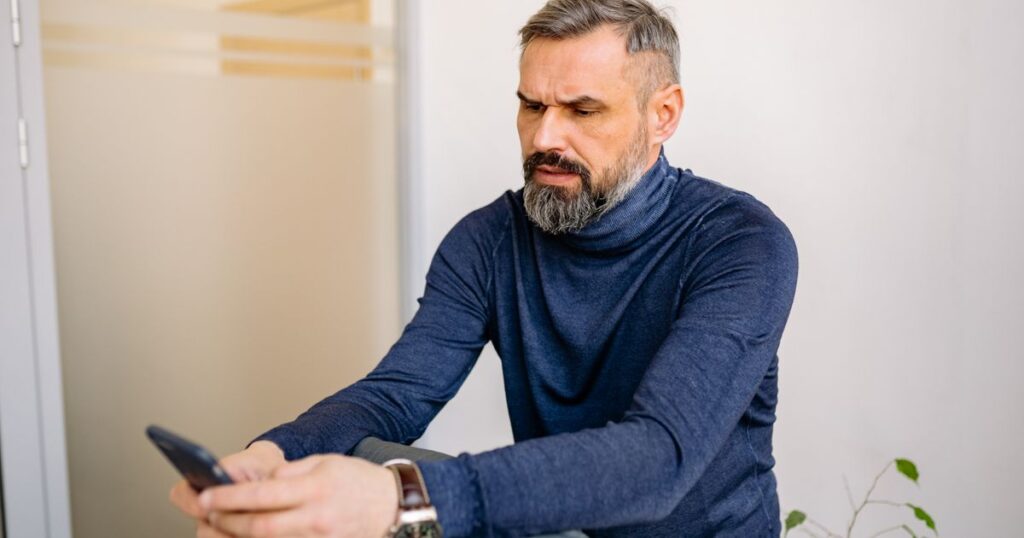 Homem consultando no celular o aplicativo do plano e descobrindo que o hospital saiu da rede credenciada