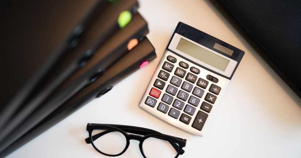 Calculadora, pastas de documentos e óculos sobre a mesa, representando contrato coletivo de plano de saúde