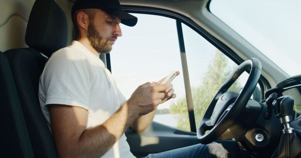 Motorista sentado ao volante conferindo o celular, tema free flow e pontos na CNH