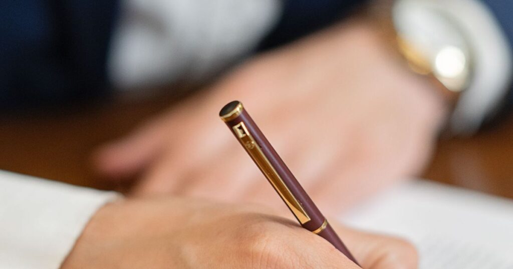 Mão assinando documento com caneta sobre a mesa