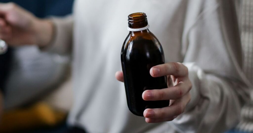 Mão segurando frasco âmbar de medicamento oral de uso contínuo em casa, o cenário do pedido do Evrysdi (risdiplam) ao plano de saúde