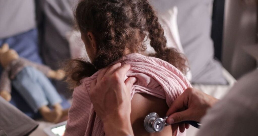 Criança de costas sendo auscultada com estetoscópio em casa, acompanhamento respiratório da fibrose cística antes de pedir o Trikafta ao plano de saúde