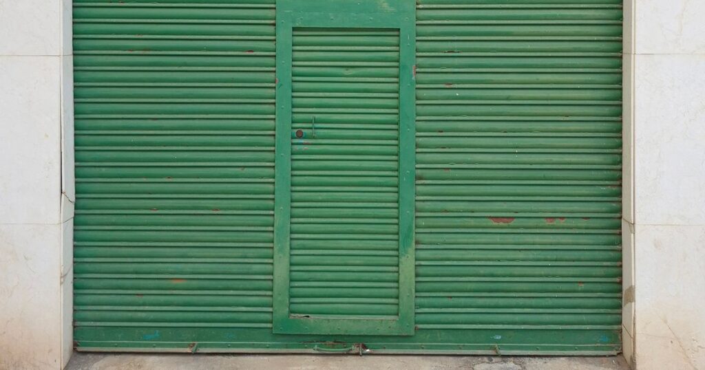 porta de aço abaixada numa loja fechada, representando a empresa que parou de funcionar sem dar baixa no CNPJ