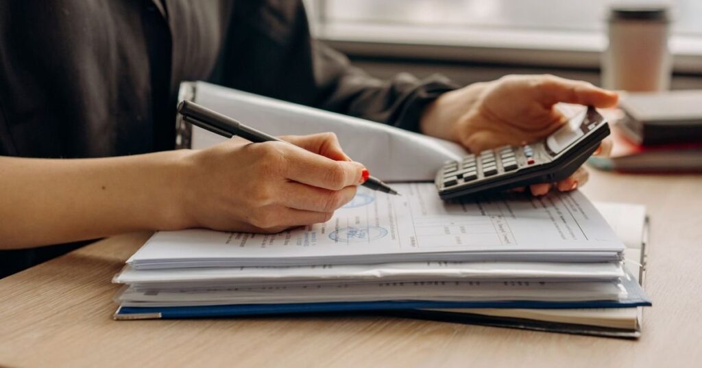 Juros abusivos em empréstimo empresarial: financeiro da empresa revisando o contrato de capital de giro com calculadora e pasta de documentos