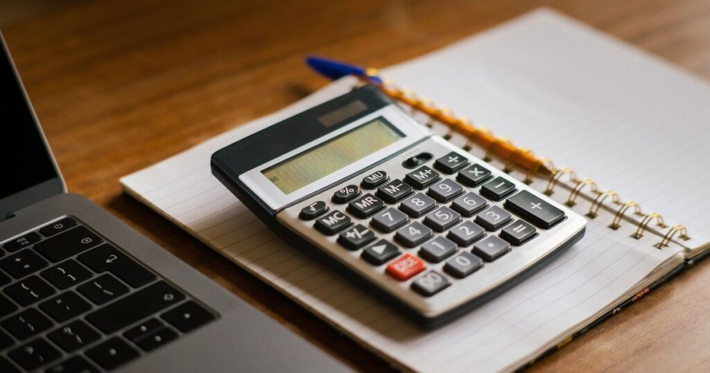 Calculadora sobre um caderno aberto ao lado de um notebook, na conta da parcela antes de renegociar o Pronampe atrasado da empresa