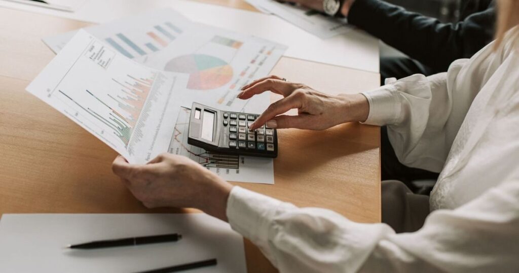 Dono de empresa analisando relatórios financeiros com calculadora para entender a renovação de capital de giro e o crescimento da dívida