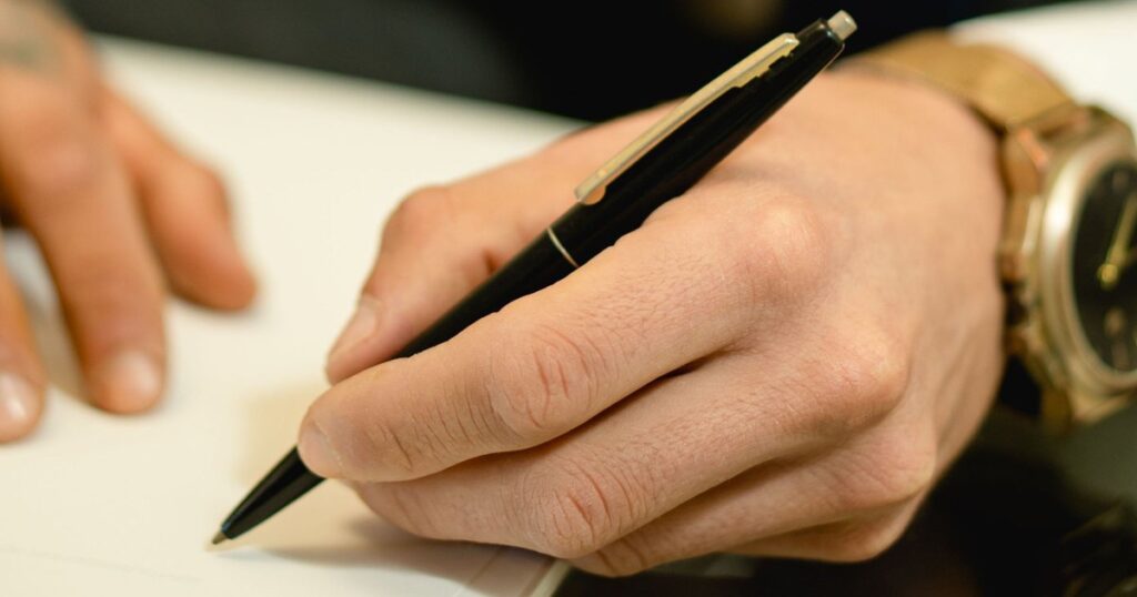 Mão do sócio avalista assinando com caneta a garantia da dívida da empresa com o banco