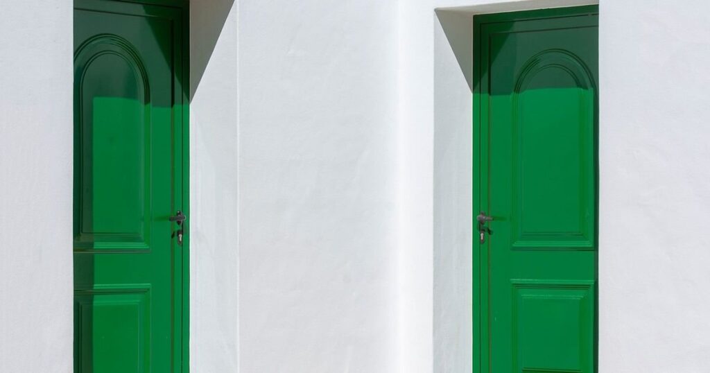 Duas portas verdes iguais, lado a lado, numa parede branca, ilustrando o ex-sócio que abriu empresa concorrente no mesmo ramo